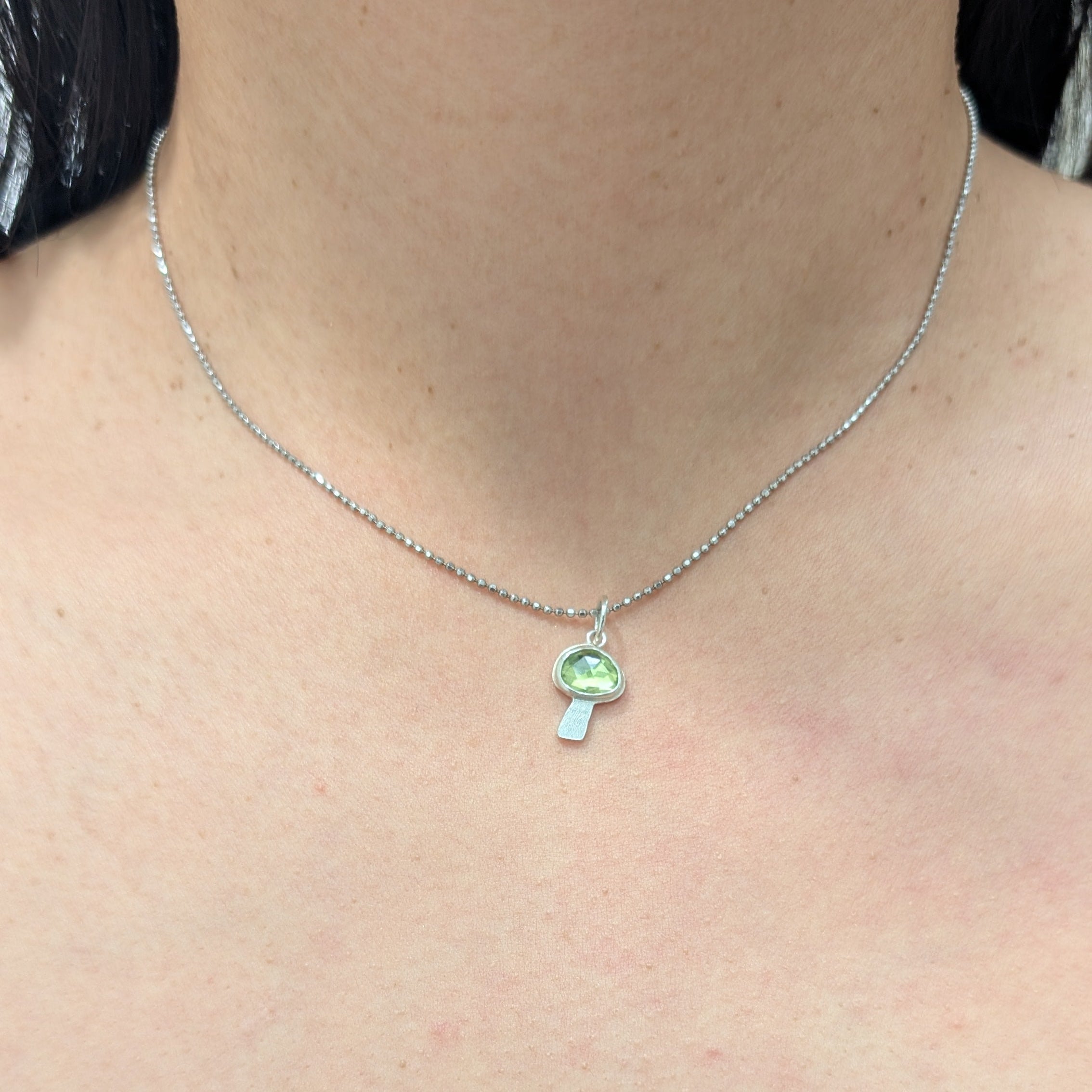 Necklace with a peridot mushroom pendant worn by a person