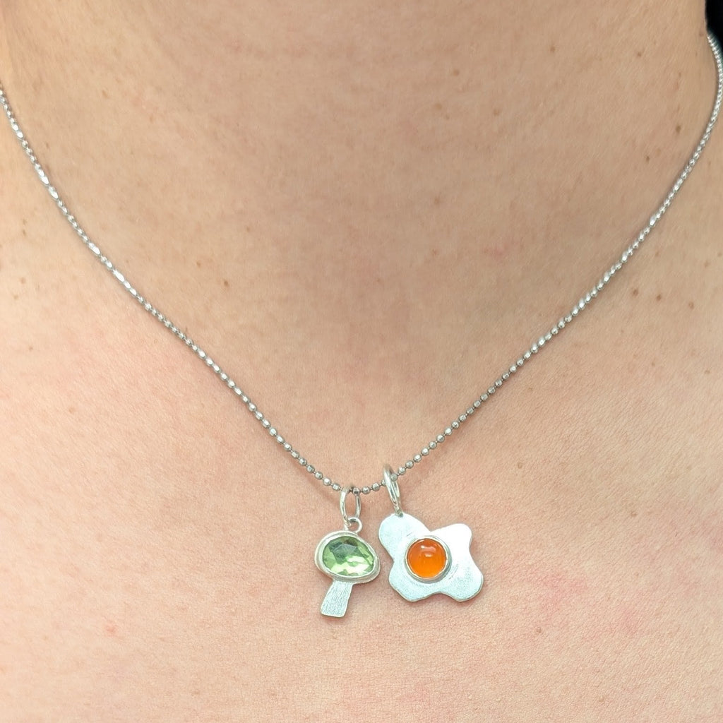 Necklace with a fried egg pendant and mushroom pendant worn by a person