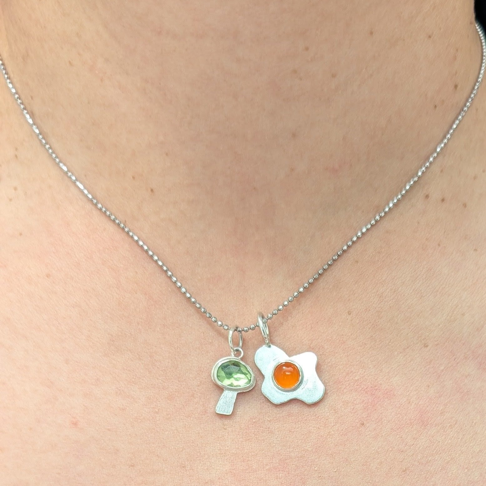 Necklace with a fried egg pendant and mushroom pendant worn by a person