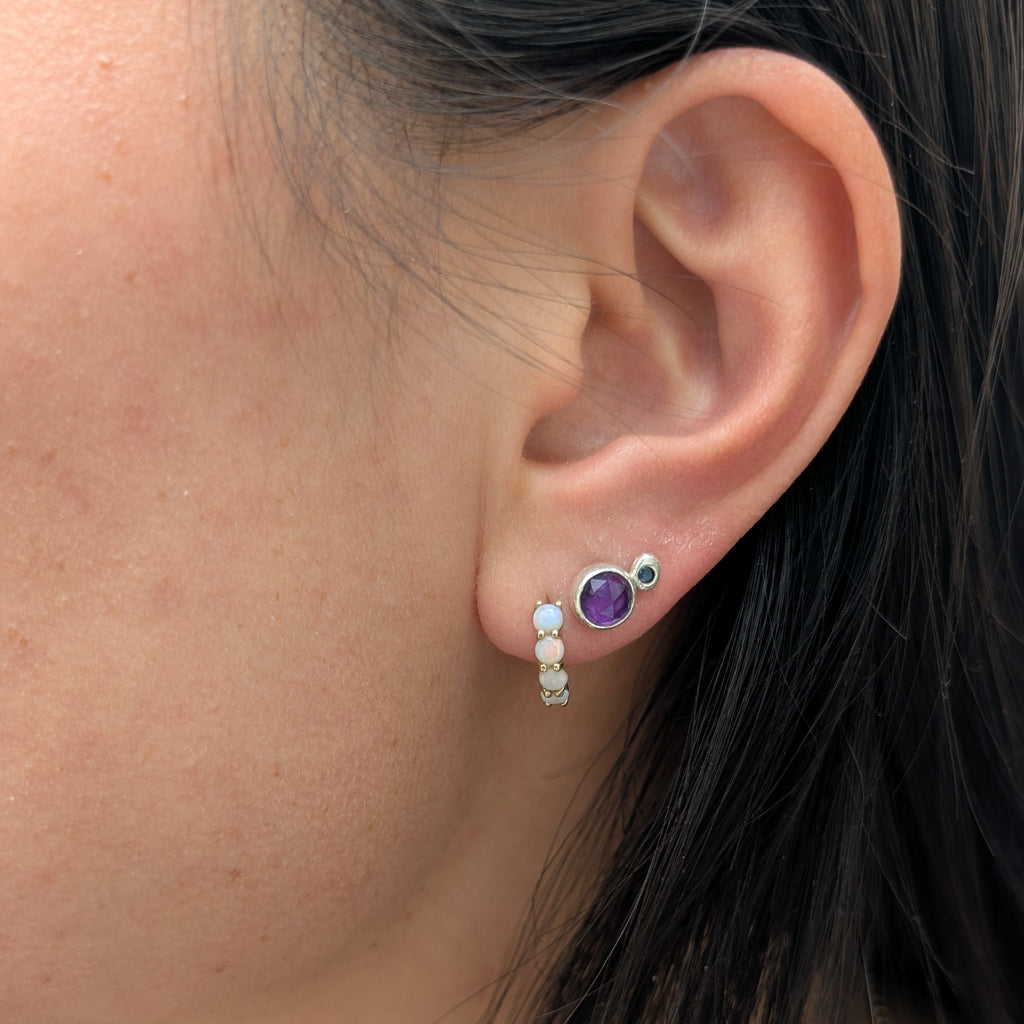 Close-up of an ear wearing a silver earring with a purple gemstone.