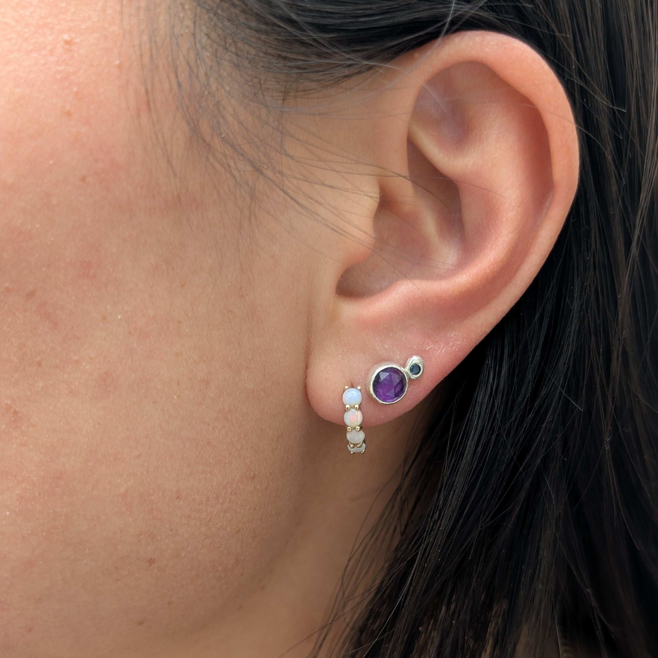 Close-up of an ear wearing a silver earring with a purple gemstone.