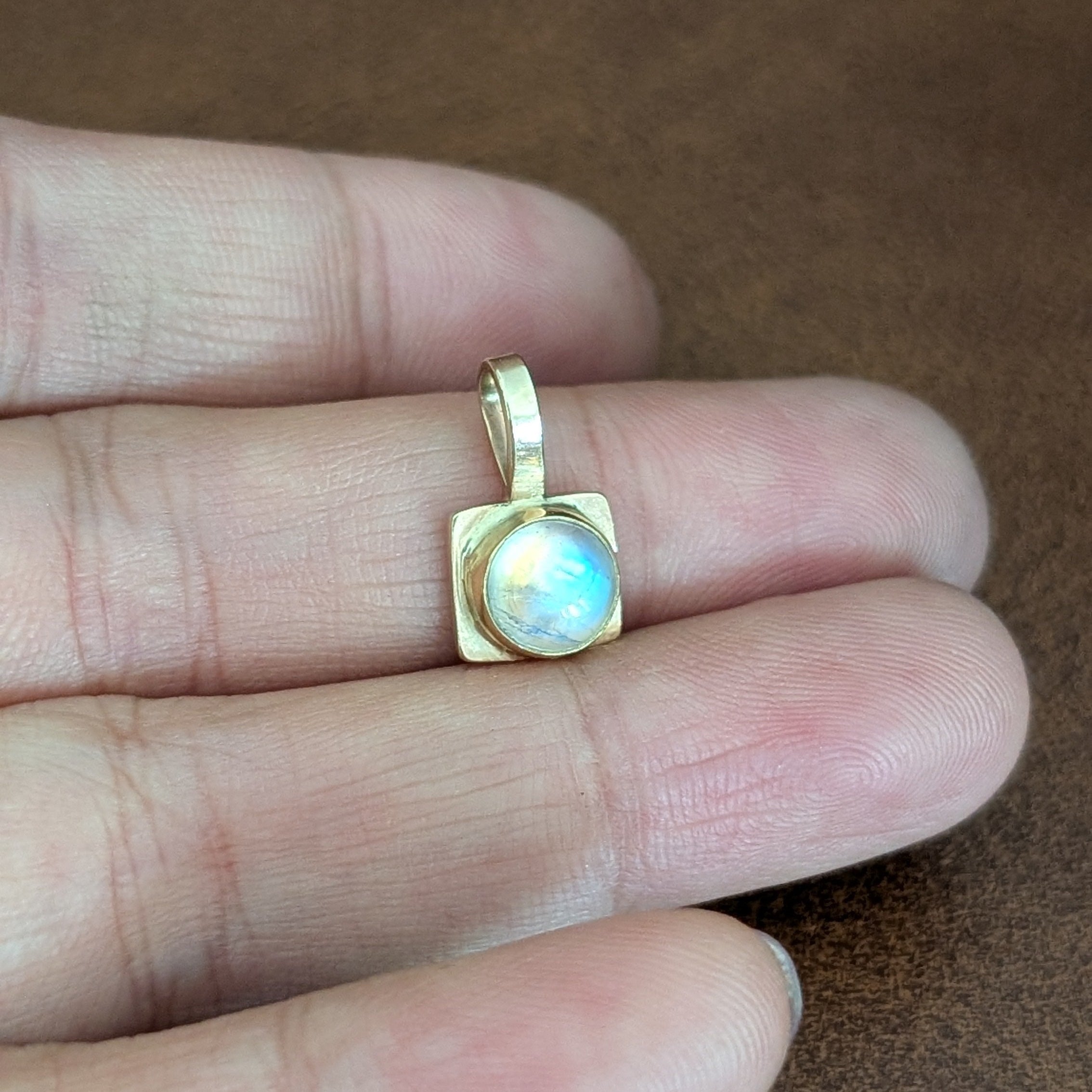 Gold pendant with a central gemstone held between fingers on a brown surface