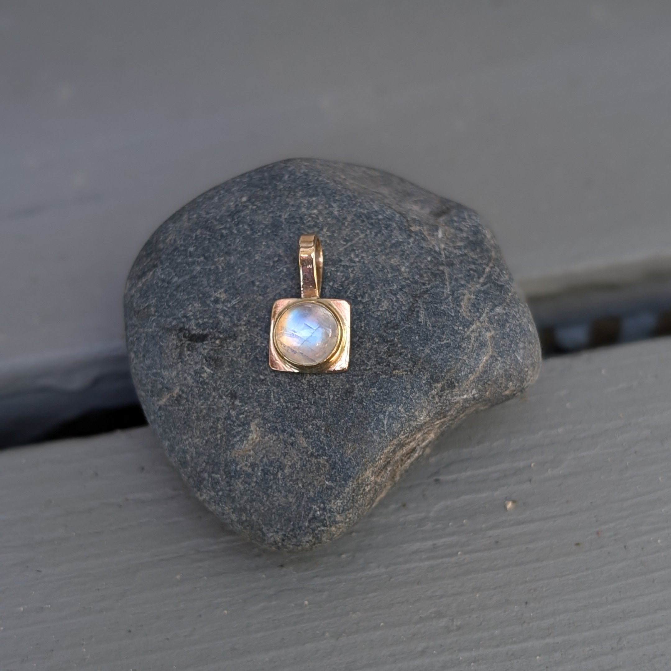 Gold pendant with a moonstone on a dark stone surface