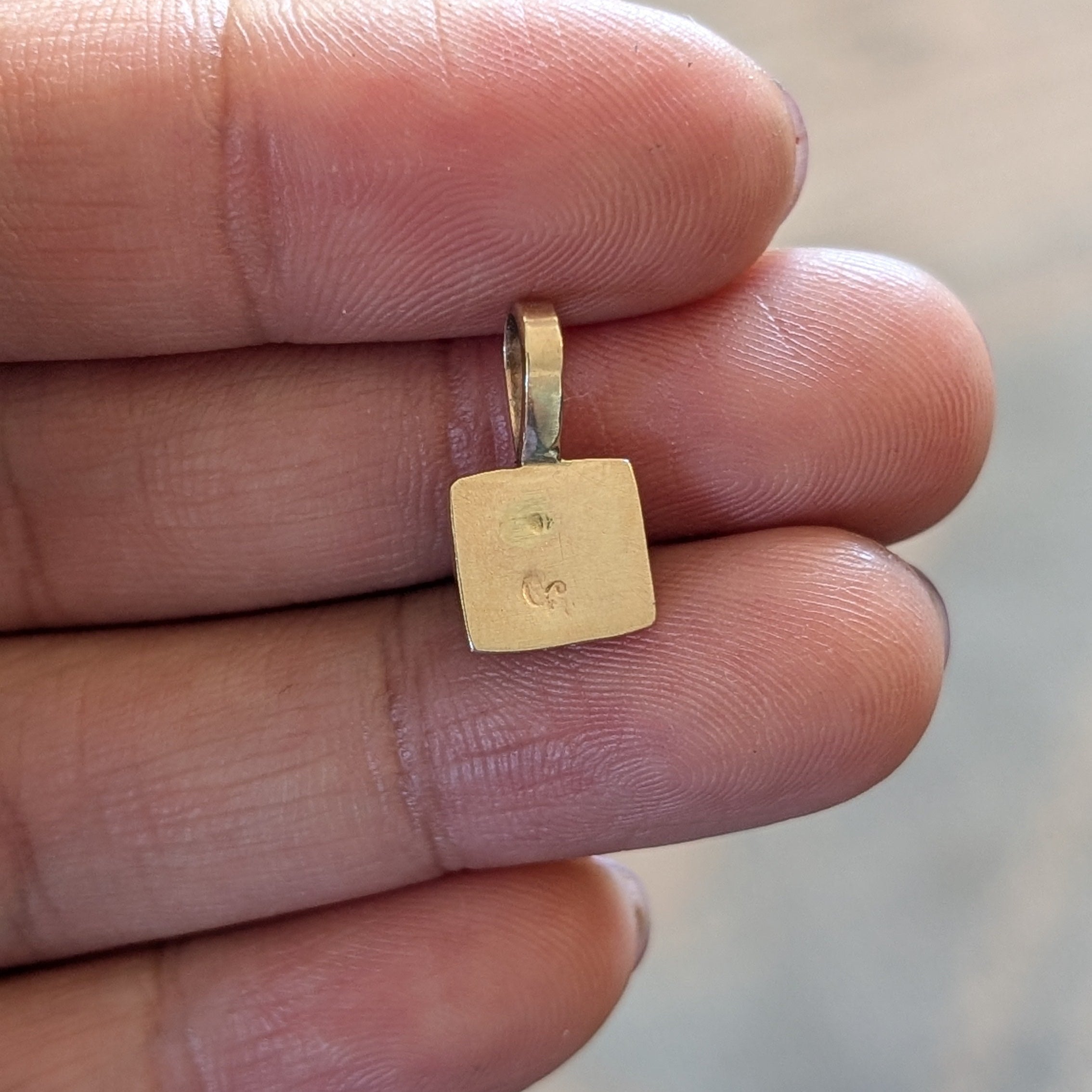 Gold pendant held between fingers with a blurred background