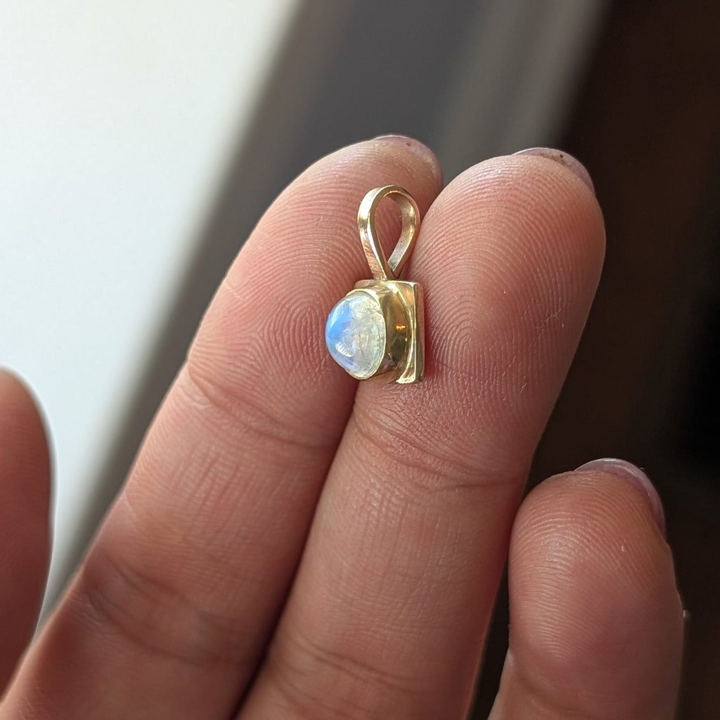 Gold pendant with a gemstone held between fingers against a neutral background