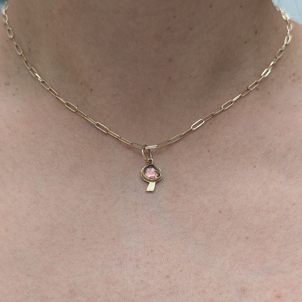 Gold necklace with a pink pendant on a person's neck against a light blue background