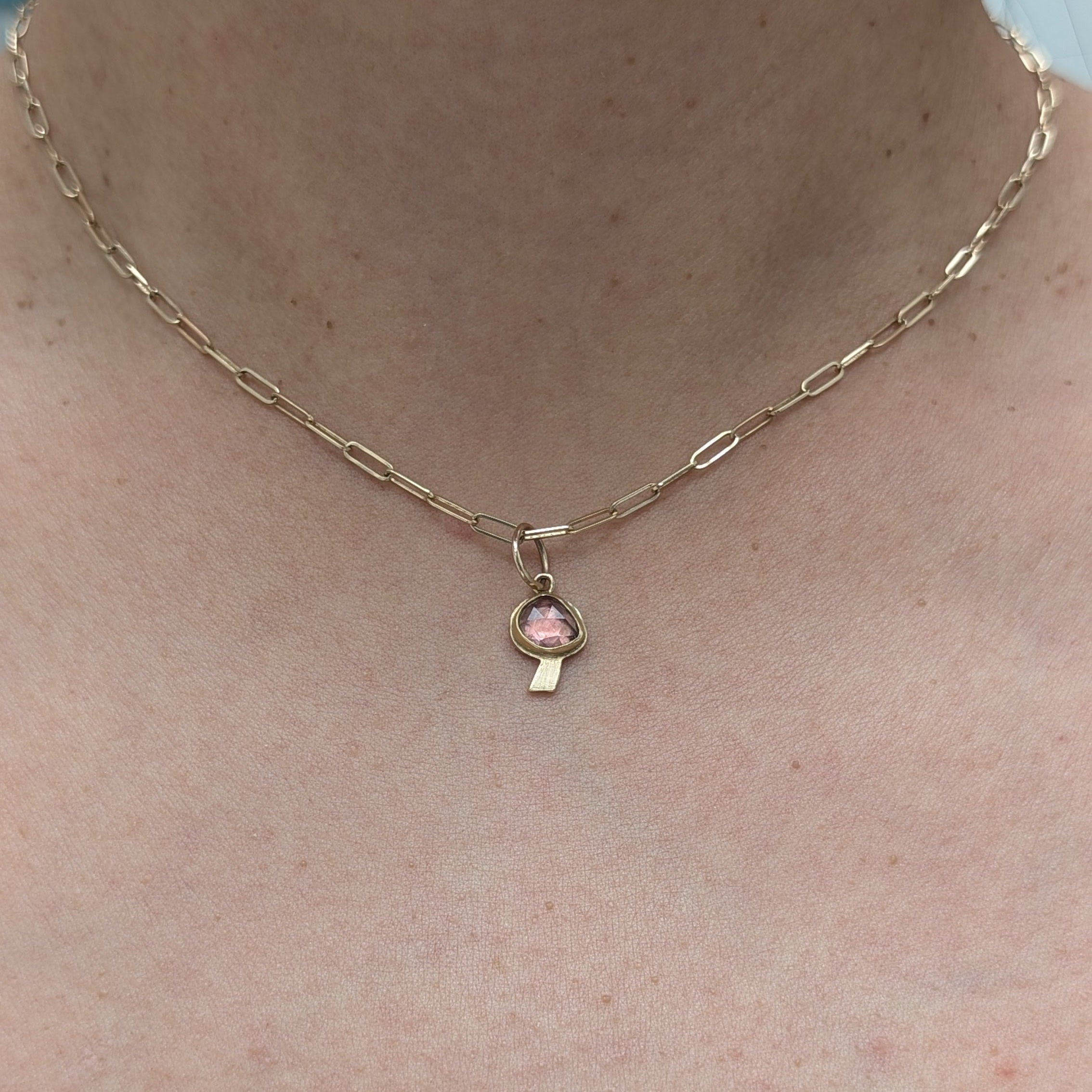 Gold necklace with a pink pendant on a person's neck against a light blue background
