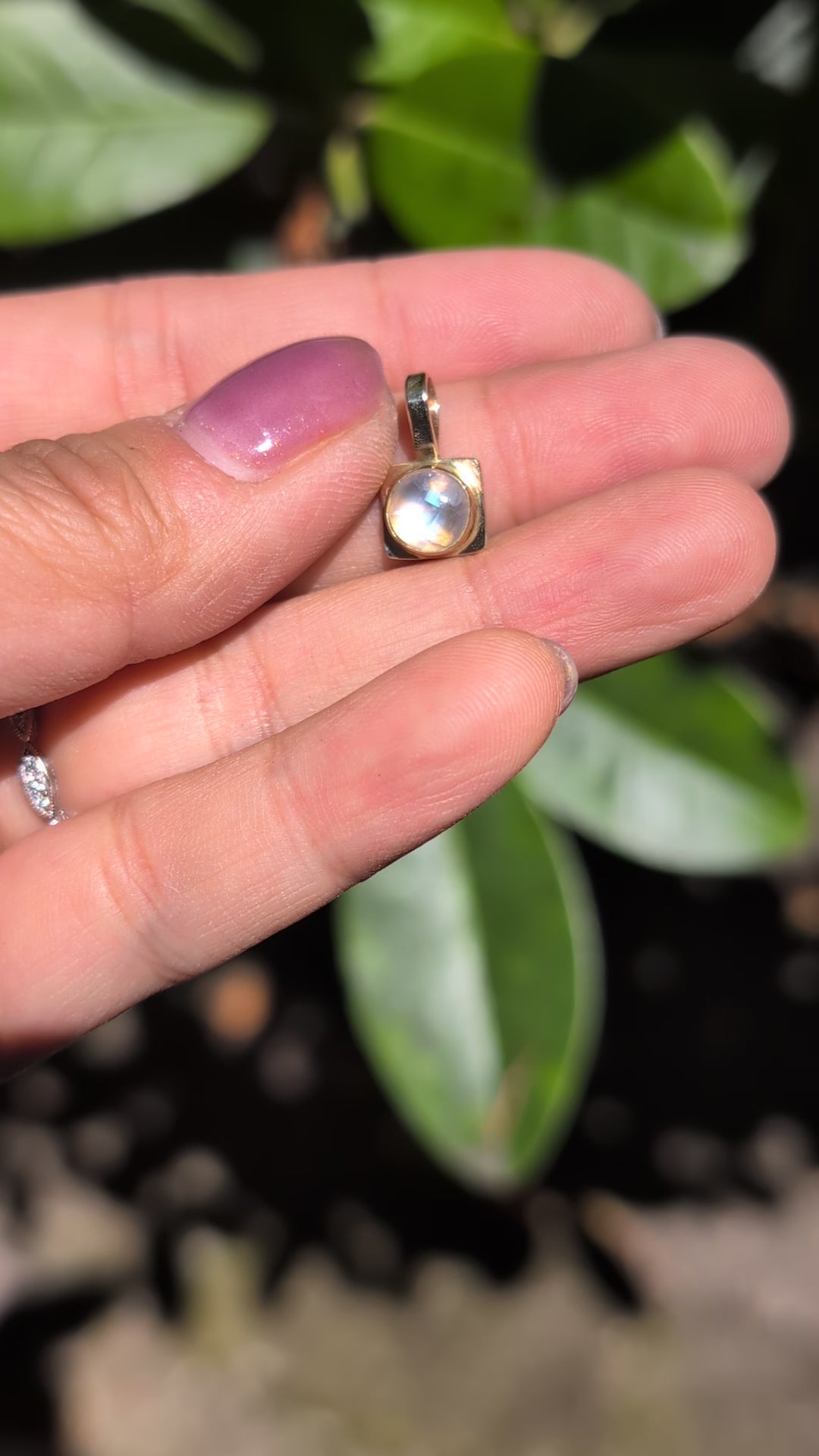 a gold and moonstone pendant held in a hand in the sunlight