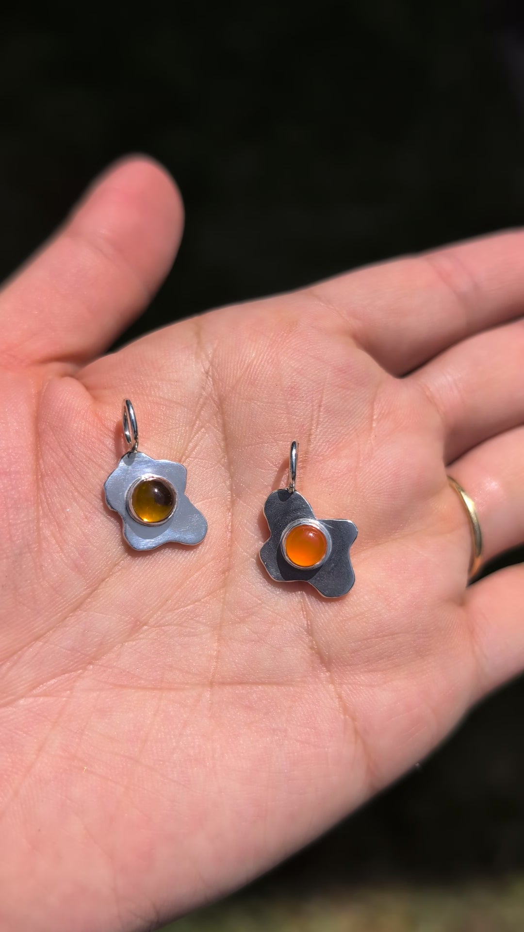 video of two fried egg pendants made of silver, one with a citrine stone and one with a carnelian stone
