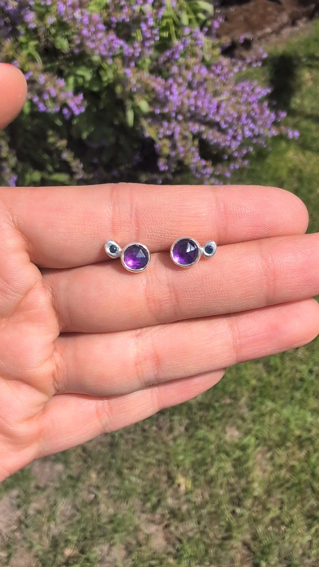 Pair of silver earrings with purple gemstones on a stone surface