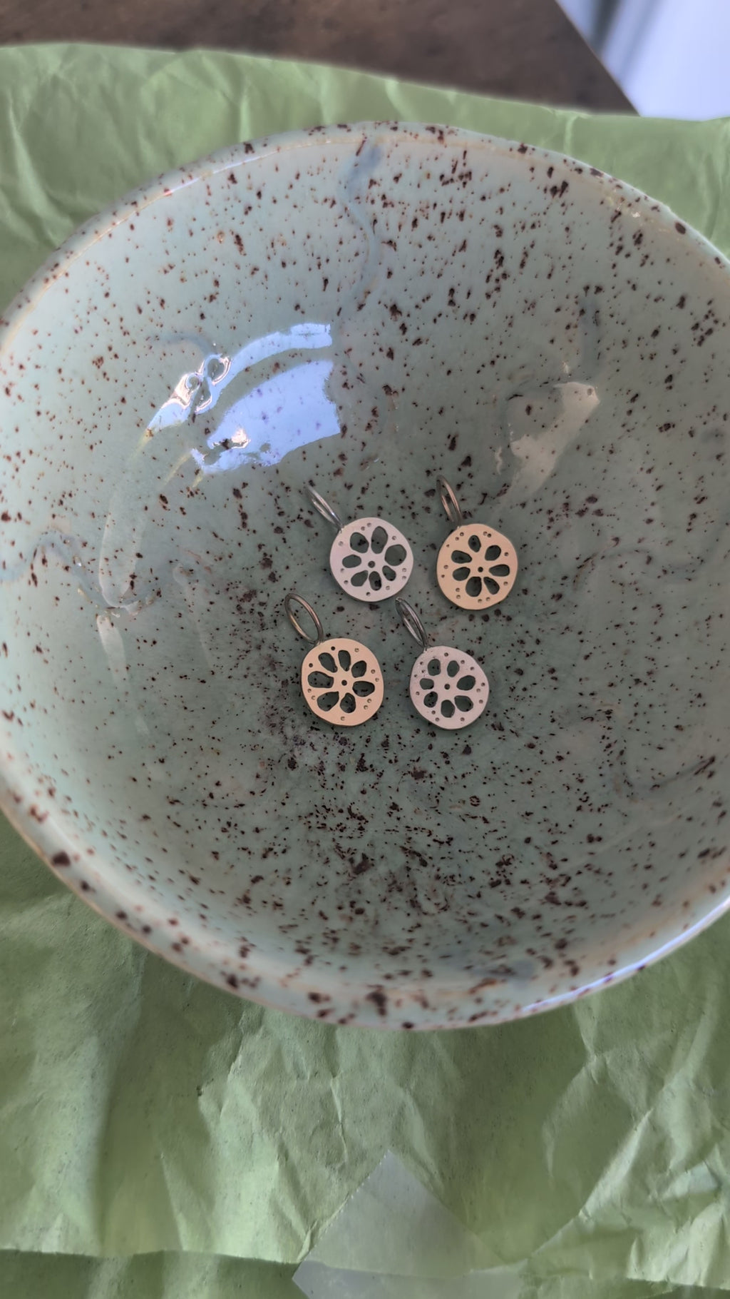 Four lotus root pendants, two gold and two silver, in a textured ceramic dish