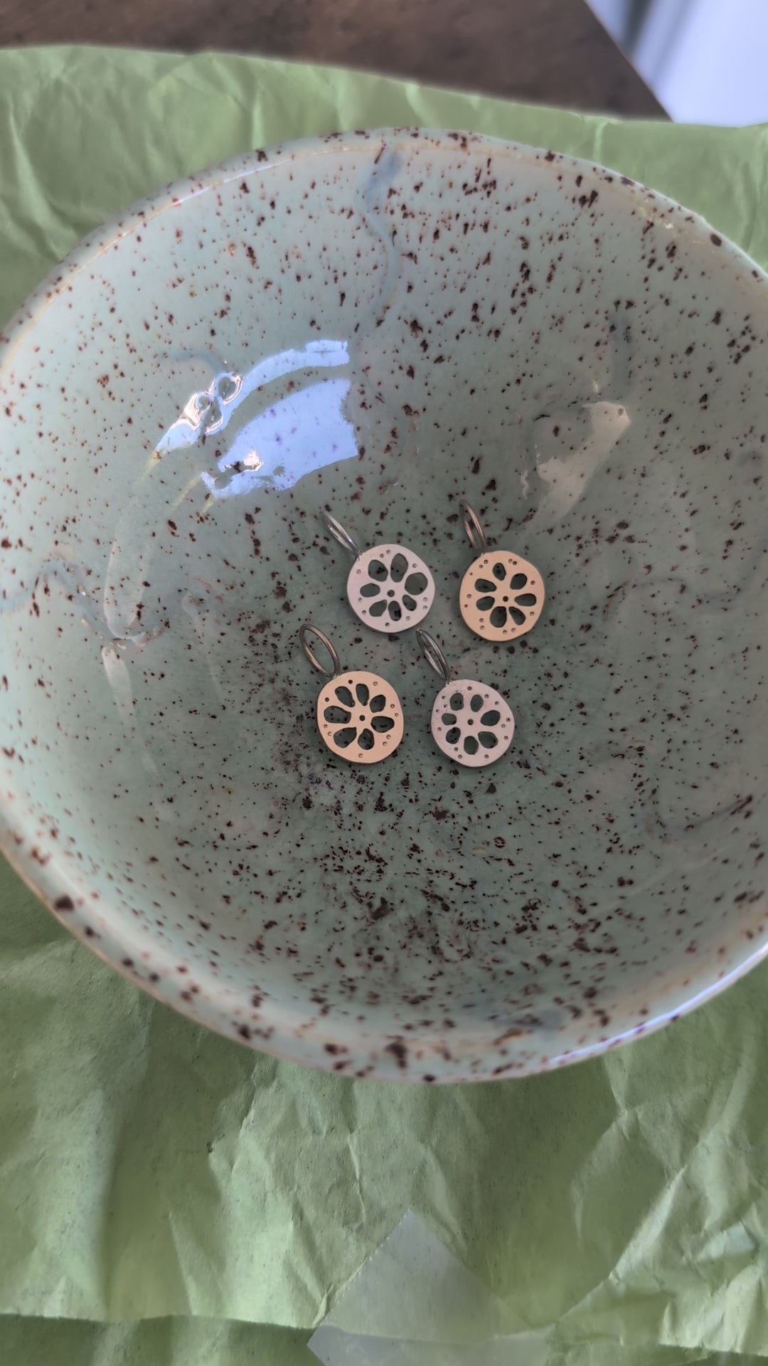 Four lotus root pendants, two gold and two silver, in a textured ceramic dish