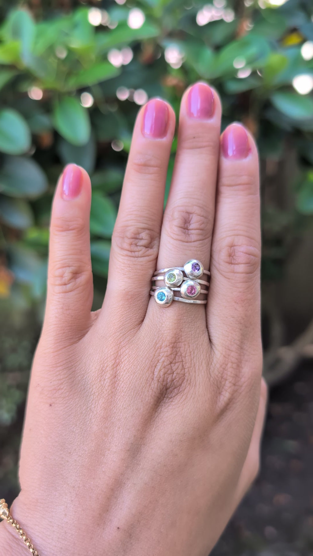 video of a hand wearing a stack of silver rings with multicolored gemstones