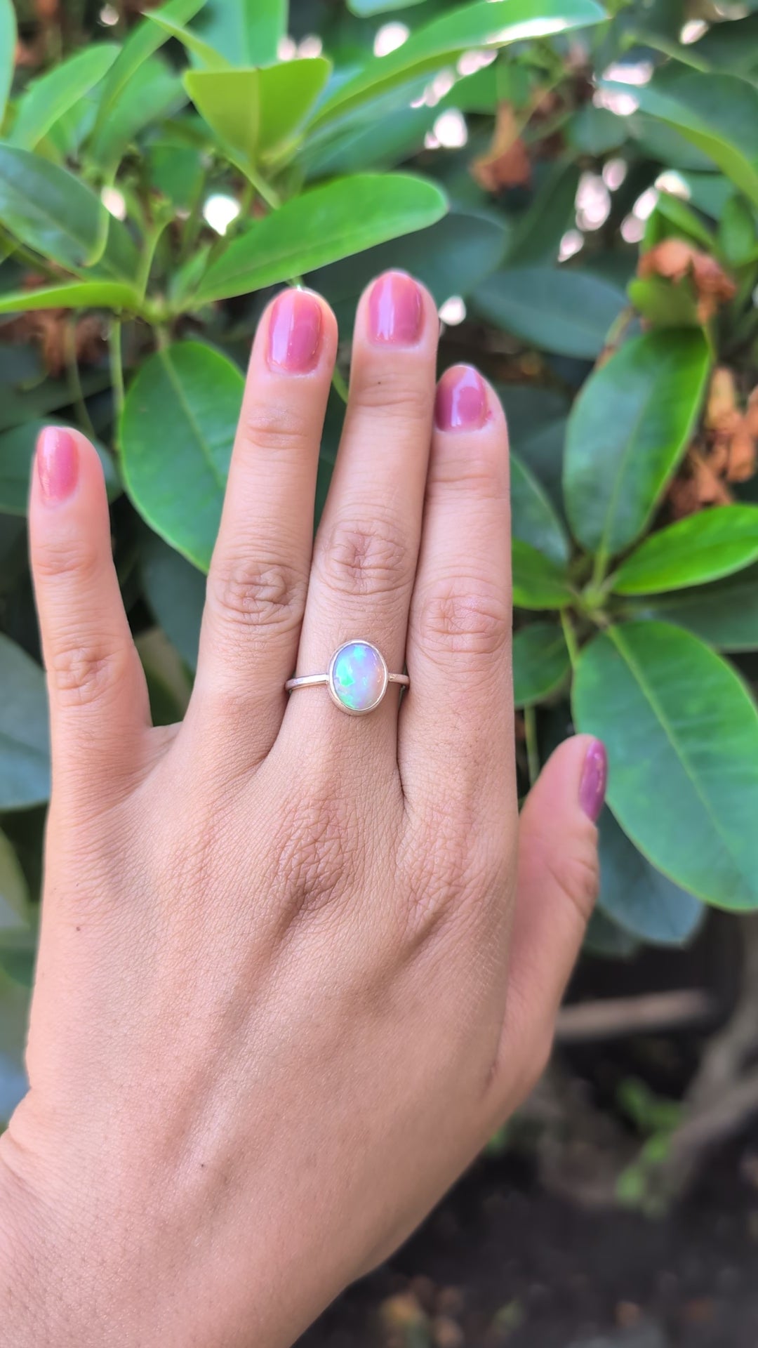 Hand wearing a ring with a colorful Ethiopian opal against a blurred natural background