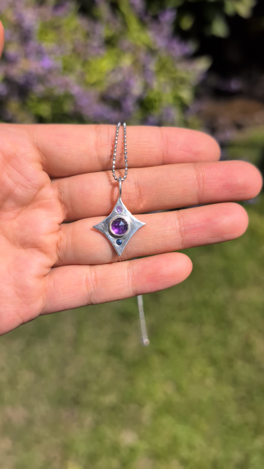 Silver star-shaped pendant with a purple gemstone held in a hand against a green background