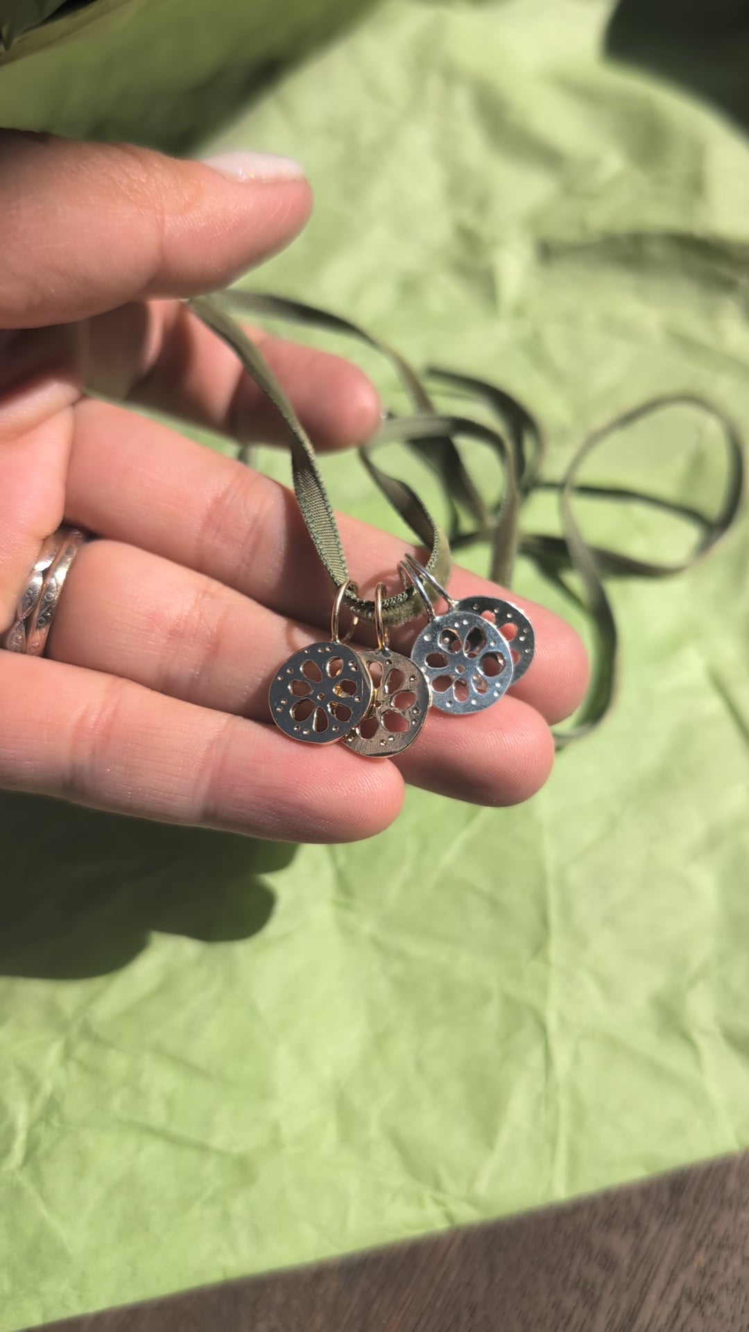 Four lotus root pendants, two gold and two silver, hanging from a thin green cord, displayed on a textured green surface.