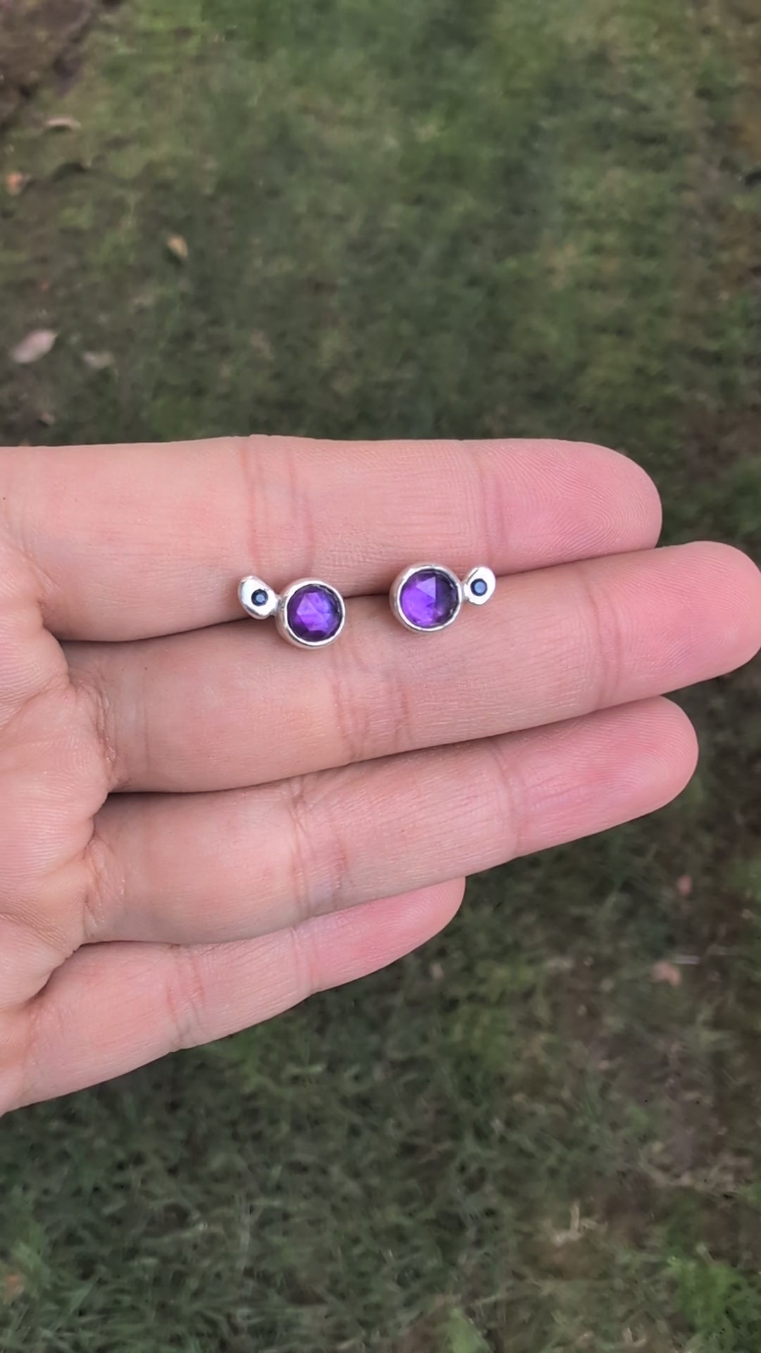 Pair of silver earrings with purple gemstones on a stone surface