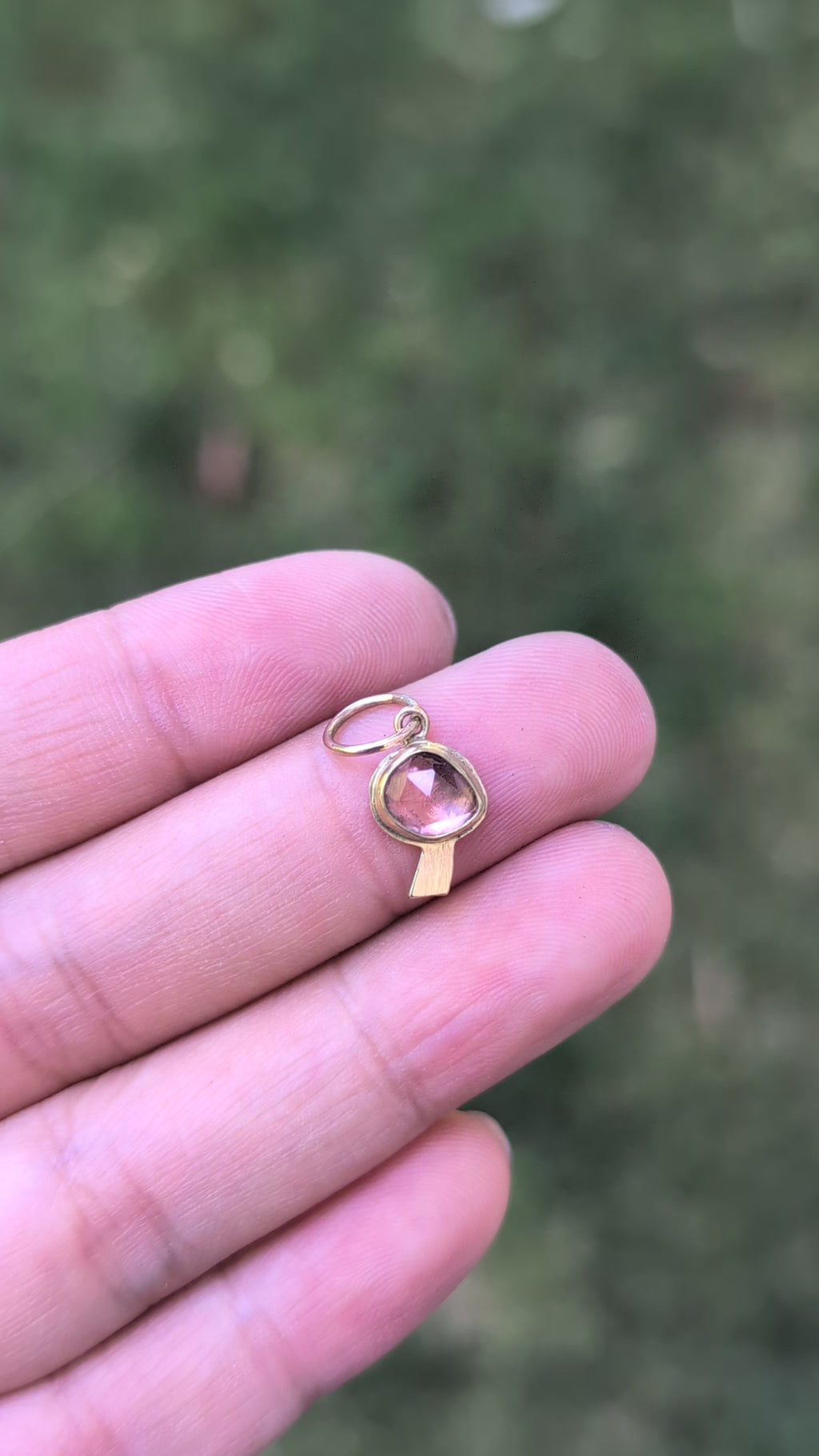 video of a gold mushroom-shaped charm with a pink gemstone