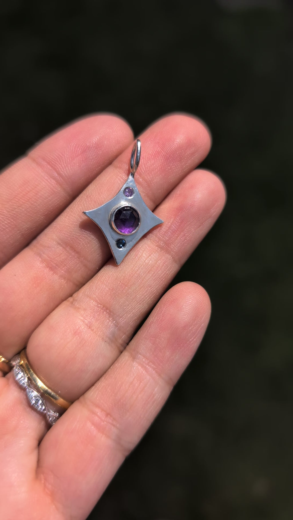 Silver star-shaped pendant with a purple gemstone held in a hand against a green background